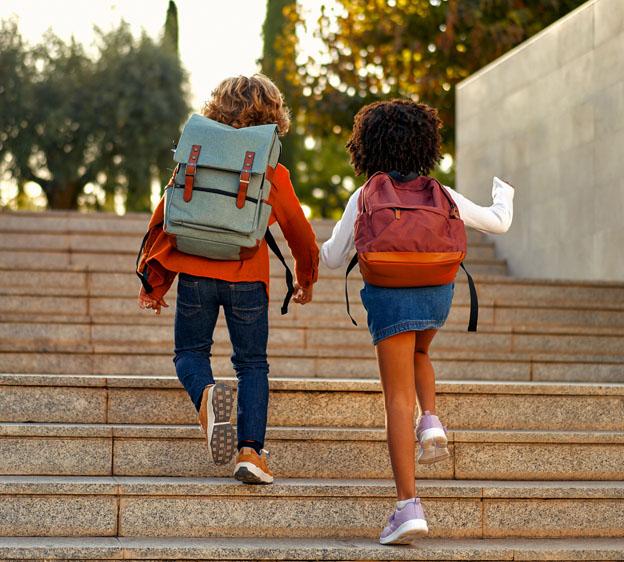 Two children, wearing backpacks, walk up steps